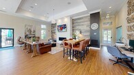 Located at 55 Dorset Crossing Drive in Simsbury, Connecticut, this single-floor community lounge space offers a well-appointed, open-plan layout combining a kitchen and living area. The living room is anchored by a striking floor-to-ceiling accent wall clad in weathered wood-look planks, complemented by a sleek linear fireplace set in a white stacked-stone surround. Warm hardwood flooring runs throughout, and elevated ceilings with crown molding contribute to an airy, welcoming atmosphere. Multiple seating arrangements—including lounge chairs, a sofa, and bar-height dining tables with leather chairs—make the space highly functional and social. A wall-mounted television above the fireplace adds a media focal point. The kitchen is equally impressive, featuring dark cabinetry, a luminous white countertop, full-height subway tile backsplash, stainless steel appliances, and open floating shelves. Pendant lights hang above the central island, while a generous bank of windows floods the kitchen with natural light and offers views of the surrounding landscape. A dedicated coffee station and a secondary dining nook with a wall-mounted TV provide additional functionality. Overall, the space blends contemporary design with a warm, inviting ambiance ideal for gathering and relaxation.