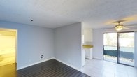 This single-floor space offers a clean and functional layout designed for comfortable everyday living. The main living area features durable wood-look laminate flooring and is finished with light grey walls and white baseboards, creating a neutral and versatile backdrop. A textured popcorn ceiling adds a classic touch overhead, while a wall-mounted vent ensures efficient climate control throughout the space.

The living area flows seamlessly into the kitchen, which is separated by a partial wall. The kitchen is outfitted with white cabinetry, a bright yellow countertop that adds a pop of color, and white appliances, giving it a clean and practical feel. Light tile flooring in the kitchen area contrasts neatly with the laminate in the living space, clearly defining each zone.

Natural light fills the interior through a glass sliding door that leads to an outdoor area, enhancing the overall sense of openness. The transition between the living space and the outdoor access area is smooth, making the connection to the exterior a notable feature of the layout. Overall, this space presents a straightforward, well-maintained environment with a bright and airy ambiance suited to a variety of uses.