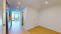 Located at 632 Newark Avenue in Jersey City, NJ, this modern studio offers a thoughtfully designed single-floor layout that maximizes every square foot. The living area is anchored by expansive floor-to-ceiling windows that frame breathtaking views of the New York City skyline, flooding the space with natural light and creating an open, airy atmosphere. Light-toned hardwood flooring runs throughout, complementing the clean, minimalist aesthetic defined by crisp white walls and recessed lighting.

The galley-style kitchen is outfitted with contemporary blue-grey cabinetry, a subway tile backsplash, stainless steel appliances including a range and microwave, and a single-basin sink — combining style with practical functionality. A hallway connects the main living areas to a dedicated laundry space and two closets, providing ample storage for a compact unit.

The bathroom is finished to a high standard, featuring large-format white tiles, a glass-enclosed walk-in shower, a wall-mounted vanity with an undermount sink, and an illuminated mirror cabinet. The overall design of the space is modern and cohesive, with neutral tones and quality finishes throughout that reflect a polished urban living experience ideally situated near the vibrant amenities of Jersey City.