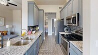 This single-floor residence offers a thoughtfully designed layout that balances style and functionality across its key living spaces. The galley-style kitchen is a standout feature, showcasing slate-blue shaker cabinetry, granite countertops, a double stainless steel sink, a mosaic tile backsplash, and a full suite of stainless steel appliances including a refrigerator, electric range, and over-the-range microwave. Wood-look plank flooring runs throughout, providing a cohesive and modern aesthetic.

The living room is bright and welcoming, featuring elevated ceilings, a ceiling fan, and large windows that allow natural light to fill the space. The neutral warm-gray color palette creates a calm and inviting ambiance throughout.

The space includes two bedrooms, each equipped with a ceiling fan and windows offering natural light. One bedroom features a more spacious layout with a dresser alcove, while the other offers a cozy, intimate feel with a tufted upholstered headboard as a focal point.

The full bathroom is elegantly finished with a granite-topped blue vanity, wood-look flooring, and an arched-niche tub and shower combination with tile surround. A dedicated in-unit laundry closet with side-by-side washer and dryer and built-in shelving adds everyday convenience to this well-rounded residence.