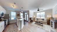 Located at 11 Parklands Drive in Bluffton, South Carolina, this single-floor residence offers a thoughtfully designed open-concept layout that seamlessly connects the kitchen and living areas. The kitchen is a standout feature, showcasing crisp white shaker cabinetry, light quartz countertops, and a subway tile backsplash. A generously sized island with bar seating provides both additional workspace and a natural gathering spot. Stainless steel appliances, including a French door refrigerator, electric range with microwave, and dishwasher, complete the modern culinary setup. Pendant lighting and a track light fixture illuminate the space with style, while large windows allow abundant natural light to pour in throughout the day. The adjoining living area flows naturally from the kitchen, featuring light hardwood-style flooring, crown molding, and a ceiling fan. Multiple windows frame views of the surrounding neighborhood, maintaining a bright and airy atmosphere. A dedicated utility area includes wire shelving for storage, washer and dryer hookups, and a built-in pet door, offering practical convenience. Neutral wall tones and consistent flooring throughout the home create a cohesive, modern aesthetic well-suited to the Lowcountry lifestyle of Bluffton, SC.
