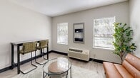 Located at 950 Travelers Blvd in Summerville, SC, this efficiently designed studio unit offers a smart, functional layout across a single floor. The open living area is finished with light wood-look luxury vinyl flooring and neutral gray-toned walls, creating a bright and clean aesthetic throughout. A tan leather futon sofa, glass-top coffee table, and a wall-mounted decorative mirror anchor the living space, while two windows fitted with horizontal blinds allow ample natural light to fill the room. A wall-mounted HVAC unit provides climate control directly in the living area. The kitchenette is smartly integrated into the space, featuring dark cabinetry, a stainless steel full-size refrigerator, a compact microwave, open shelving, and a single-basin sink with bar-height seating for dining. A built-in coat and storage nook near the entry adds practical organization. The bathroom is generously proportioned for the unit's scale, outfitted with light vinyl flooring, a soaking tub, a curtained shower area, wall-mounted grab bars for accessibility, a wall-mounted medicine cabinet, and a toilet. Textured ceilings are consistent throughout. This unit offers a clean, modern, and highly functional design well-suited for short- or extended-stay occupancy.