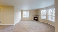This single-story residence is thoughtfully laid out across a functional and connected floor plan. The living room serves as the centerpiece of the home, offering a generously sized, carpeted space bathed in natural light from multiple windows fitted with white blinds. A corner fireplace with a tile surround and a modest mantel provides a warm focal point, adding both visual interest and comfort to the room.

Adjacent to the living area is a dining space that transitions seamlessly toward the kitchen, benefiting from an additional window and a private exterior door that allows for easy outdoor access. The kitchen is well-appointed with white cabinetry offering ample storage, dark laminate countertops, a stainless steel gas range, a built-in microwave, a stainless steel refrigerator, a dishwasher, and a single-basin sink. Light tile flooring and overhead fluorescent lighting make the space bright and practical.

The bathroom features a full tub-and-shower combination with white tile surround, a toilet, and tile flooring. Stainless steel grab bars are installed for added accessibility and safety. Throughout the home, warm beige tones create a cohesive, neutral palette that lends a clean and inviting ambiance.