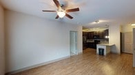 Located at 1040 Wake Towne Dr in Raleigh, NC, this single-floor residence offers a well-designed open-concept layout that seamlessly connects the living area to the kitchen. The living space features warm hardwood-style flooring and a ceiling fan with a built-in light fixture, providing both comfort and functionality. Neutral-toned walls and clean white trim contribute to a bright, welcoming atmosphere throughout.

The kitchen is outfitted with dark espresso cabinetry, black appliances including a refrigerator and microwave, and a kitchen island or peninsula that offers additional counter space and a natural division between the cooking and living areas. Track lighting mounted on the kitchen ceiling ensures ample illumination for meal preparation. The overall color palette of deep cabinetry contrasted against lighter countertops and walls gives the kitchen a modern, polished look.

A doorway visible from the main living area leads to additional rooms within the residence, suggesting a functional floor plan designed to maximize usability. The cohesive design elements — including consistent flooring, coordinated fixtures, and a neutral color scheme — create a unified and inviting living environment suitable for everyday comfort.
