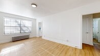 Located at 1410 Monroe Ave in Rochester, NY, this single-floor, two-bedroom unit offers a well-organized layout comprising a living room, two bedrooms, a kitchen, and two hallways. Throughout the space, light-toned hardwood flooring creates a cohesive, bright aesthetic that complements the consistently white walls and clean white trim.

The living room is a comfortable, open area that benefits from multiple windows fitted with blinds, allowing natural light to fill the space. Classic cast-iron radiators are present in several rooms, a hallmark of the building's traditional construction, providing reliable heating. The primary bedroom is a well-proportioned room featuring multiple windows and direct access to a kitchen, which showcases white cabinetry, light countertops, a gas range, and a distinctive light-blue subway tile backsplash that adds a touch of character to the otherwise neutral palette.

The second bedroom is a more compact but functional space with its own window and radiator. A bedroom closet features sliding panel doors with a built-in hanging rod. Two hallways connect the rooms efficiently. Overall, the unit maintains a clean, updated appearance with consistent finishes throughout.