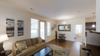This single-story Highland residence offers a well-designed two-bedroom, two-bathroom layout that makes efficient use of its space. The open-concept living and dining area serves as the heart of the home, featuring warm hardwood flooring that extends throughout the main living spaces. Large windows with blinds allow generous amounts of natural light to fill the room, creating a bright and welcoming atmosphere with views of the surrounding greenery outside.

The living area provides ample room for comfortable seating arrangements, complemented by clean white walls and smooth ceilings with recessed ventilation. The dining area flows naturally from the living space and is defined by an elegant chandelier overhead, adding a refined touch to the open floor plan. A decorative mirror with a textured mosaic frame adorns the dining area wall, enhancing the sense of depth and style in the space.

A glimpse into the adjacent bedroom reveals continued use of consistent flooring and neutral tones, maintaining a cohesive aesthetic throughout. The overall design balances functionality with a clean, modern sensibility, making this a practical and comfortable two-bedroom residence.