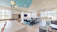 Located at 1305 Central Ave in Charlotte's dynamic Plaza Midwood neighborhood, this single-floor community lounge is a thoughtfully designed social hub. The open-plan layout is anchored by herringbone-patterned wood-look flooring that flows seamlessly throughout the entire space, lending warmth and visual continuity.

The main lounge area is generously proportioned, featuring multiple distinct seating zones. A large sectional sofa paired with teal-accented occasional chairs and a patterned area rug forms the central gathering spot, complemented by a mounted flat-screen TV. A cozy secondary lounge area showcases rich brown leather Chesterfield sofas set against a striking whitewashed shiplap feature wall with wall-mounted pendant lighting.

A kitchenette zone sits beneath a bold teal recessed ceiling detail, fitted with a quartz-topped bar counter, orange accent bar chairs, and a beverage station. Floor-to-ceiling windows on multiple walls flood the space with natural light and offer sweeping views of the Charlotte skyline and surrounding neighborhood. A shuffleboard table and an oversized Scrabble board add a playful recreational dimension to the space.

The hallway connects to two ADA-compliant restrooms, each finished with herringbone tile flooring and contrasting wall tile — one with dark mosaic tile and one with crisp white tile — both outfitted with grab bars and clean, modern fixtures.