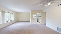 This single-floor residence offers a thoughtfully arranged layout that balances open communal spaces with private rooms. The expansive living area serves as the centerpiece of the unit, finished with neutral-toned wall-to-wall carpeting and painted in soft cream tones that enhance the sense of brightness. A ceiling fan with integrated lighting provides both comfort and illumination, while large windows along one wall invite natural light and offer views of surrounding greenery.

The kitchen is accessible via an open pass-through and doorway, creating a connected feel between the living and cooking spaces. It features gray shaker-style cabinetry with brushed gold hardware, marble-look countertops, a white subway tile backsplash, light wood-look vinyl flooring, a gold-toned undermount sink, and white appliances including a refrigerator, range, microwave, and dishwasher.

The bedroom is generously sized with soft carpet, cream-painted walls, and a window with outdoor views, offering a calm and comfortable retreat. The bathroom is well-finished with white cabinetry, a double vanity, a round mirror, sage green tile wainscoting, a mosaic tile floor, and a separate water closet area, combining classic style with functional design throughout.