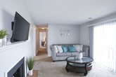 This single-floor residence offers a well-organized layout with distinct living, dining, kitchen, and sleeping areas. The living room serves as the central gathering space, featuring a wood-burning fireplace with a tiled hearth and a white mantle, plush carpeting, and a sliding glass door that opens to a private balcony, allowing natural light to fill the room. The neutral gray walls and soft carpet create a calm, cohesive atmosphere throughout.

Adjacent to the living room, the dining area accommodates a full dining set and benefits from two windows that bring in additional natural light. The kitchen features white cabinetry, a double sink, hardwood-style flooring, and black appliances including a range and refrigerator, providing a functional and clean workspace.

The hallway connects to the bedrooms and bathrooms, transitioning to rich hardwood-style flooring. The primary bathroom includes a soaking tub with cabinetry, while a second full bathroom offers a tub-shower combination with a white vanity. The bedrooms are carpeted and comfortably sized. Overall, the space presents a practical and inviting layout with consistent finishes throughout.