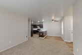 Located at 12800 SE 7th St in Vancouver, Washington, this single-floor, three-bedroom, two-bathroom home offers a functional and comfortable layout. The open-concept living and kitchen area serves as the heart of the home, featuring wood-style flooring that contrasts with plush carpeting in the living space. A ceiling fan adds comfort overhead. The kitchen is well-equipped with rich dark-brown cabinetry, stainless steel appliances including a refrigerator, range, and dishwasher, a under-cabinet range hood, and a peninsula with a white countertop — ideal for casual dining or meal prep. The primary bedroom is generously sized and connects directly to a bathroom featuring dark-wood vanity cabinetry, a white countertop, and built-in shelving with a mirrored medicine cabinet. Additional bedrooms are carpeted and offer closet storage, with one bedroom providing direct outdoor access through a glass-paneled door with natural light from multiple windows. A dedicated laundry room houses a full-size washer and dryer with a storage shelf above. The home also includes a closet with built-in shelving and a water heater. Neutral tones throughout create a clean, move-in-ready aesthetic.