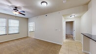 This single-story unit offers a well-organized layout connecting living, dining, and kitchen areas in a cohesive, open flow. The main living space features warm, neutral-toned carpet that transitions to light ceramic tile in the adjoining areas, with a ceiling fan providing both function and a finishing touch overhead. Natural light enters through multiple windows fitted with blinds, lending a bright, airy quality throughout.

The kitchen is a functional highlight, equipped with white cabinetry featuring detailed panel accents, dark granite countertops, and a peninsula that provides additional prep and seating space. White appliances — including a refrigerator, range, and built-in microwave — are neatly integrated, and an in-unit washer is conveniently located nearby.

The bedrooms are generously proportioned, each finished with plush carpet, ceiling fans, and windows that bring in natural light. The primary bathroom features tile flooring, a tub-shower combination with sliding glass doors, a white vanity with dark granite countertop, and a large mirror. A secondary bathroom offers a pedestal sink and toilet, finished with the same tile flooring consistent throughout the unit. The overall palette of warm beige and white tones creates a clean, cohesive ambiance.