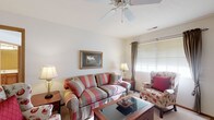 Located at 100 Glenwood Dr in Heath, Ohio, this single-floor residence offers a comfortable and functional layout with well-defined living spaces throughout. The living room is a welcoming area anchored by a ceiling fan and natural light streaming through blinded windows with decorative drapes. Soft carpeting and neutral walls create a warm, relaxed atmosphere. Adjacent to the living area, a dedicated dining space features carpeted flooring and an elegant chandelier overhead, providing an ideal setting for meals and gatherings. The kitchen is outfitted with warm oak cabinetry offering generous storage, light countertops, white appliances including a range, microwave, and refrigerator, and durable tile flooring that is easy to maintain. The bedroom is a serene retreat with plush carpeting, natural light from a window dressed with patterned drapes, and ample space for furnishings. The bathrooms are clean and practical — one includes a vanity with a wide mirror and a glass-enclosed shower, while another features a soaking tub with a curtain surround. Throughout the home, consistent finishes such as wood-tone trim, neutral walls, and coordinated fixtures contribute to a cohesive and inviting atmosphere suited for everyday living.