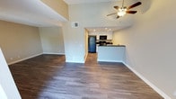 This single-story unit showcases a thoughtfully designed open-concept layout that seamlessly connects the living area to the kitchen. The living space is anchored by rich, dark hardwood-style flooring that runs consistently throughout, complemented by tall vaulted ceilings that enhance the sense of openness. A ceiling fan with integrated lighting serves as a functional focal point overhead, while neutral warm-toned walls create a clean, welcoming atmosphere. Recessed lighting and a textured ceiling add additional character to the space.

The kitchen features white cabinetry, dark granite-style countertops, and black appliances including a refrigerator, microwave, and range. A peninsula counter provides a natural division between the kitchen and living area, offering additional prep and seating space.

The bedroom is a generously proportioned, light-filled room with the same hardwood-style flooring and a textured ceiling. It connects directly to a well-appointed bathroom, which features an extended white vanity with dark granite countertops, dual mirrors, a multi-bulb vanity light fixture, and a mirrored sliding-door closet — combining practical storage with a polished, cohesive aesthetic.