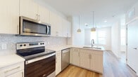 This thoughtfully designed single-floor unit offers a clean, contemporary aesthetic with a cohesive palette of whites and warm wood tones. The open-concept kitchen serves as the heart of the space, featuring white upper cabinetry, two-tone lower cabinets, a subtle tile backsplash, and bright quartz countertops. A peninsula with a built-in sink and pendant globe lighting adds both functionality and style, while a full suite of stainless steel Whirlpool appliances — including a refrigerator, electric range, over-the-range microwave, and dishwasher — ensures a well-equipped cooking environment. Light luxury vinyl plank flooring flows consistently throughout the unit, creating a seamless and easy-to-maintain surface across all rooms. The bedrooms are bright and airy, each benefiting from natural light streaming in through window blinds and ceiling fans that contribute to a comfortable, well-ventilated atmosphere. The bathroom showcases a soaking tub framed by elegant marble-patterned wall surrounds in white and grey, complemented by built-in open shelving for convenient storage. Recessed lighting throughout keeps the space feeling open and well-lit, while clean white walls and minimalist finishes lend the unit a fresh, move-in-ready quality overall.