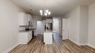 This two-story home offers a well-designed layout with consistent, modern finishes throughout. The main level centers around an open kitchen that serves as the heart of the space. White shaker-style cabinetry extends to the ceiling, providing generous storage, while granite countertops in a salt-and-pepper pattern run along the perimeter and across a central island. Stainless steel appliances, including a French door refrigerator, electric range, and over-the-range microwave, complete the kitchen. A chandelier with glass pendant shades hangs above the island, adding a refined touch. Wood-look plank flooring extends through the main living areas and entry, where a paneled door with sidelights and blinds allows natural light in. The upper level transitions to plush carpeted bedrooms, each featuring neutral walls, white panel doors, and walk-in closets with wire shelving systems. One bedroom benefits from a large window that invites natural light. A shared bathroom on the upper level is finished with a double-sink vanity topped in matching granite, white cabinetry with brushed nickel hardware, and wood-look flooring, with an adjacent walk-in closet accessible from the bathroom hallway.