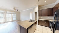 Located along Riverwalk Terrace in Jenks, Oklahoma, this single-floor, 2-bedroom, 2-bathroom home offers a thoughtfully designed layout with quality finishes throughout. The open-concept kitchen serves as the heart of the home, showcasing a granite-topped island with a built-in sink and dishwasher, rich dark-espresso cabinetry, a classic tile backsplash, and tile flooring. The kitchen flows seamlessly into the living area, which features crown molding, recessed lighting, a ceiling fan, and wood-look flooring that adds warmth to the space. Large windows allow abundant natural light to fill the living area, which also provides access to an outdoor space via French doors. The primary bedroom is generously sized, featuring plush carpet, soaring ceilings, a ceiling fan, and an expansive window arrangement that draws in natural light. The second bedroom similarly offers comfortable proportions, carpeted floors, and a ceiling fan. Each bathroom is finished with tile flooring, dark vanity cabinetry with wood-tone countertops, and a tub-shower combination accented with decorative tile detailing. A dedicated laundry room with full-size washer and dryer connections adds everyday convenience, while two closets and a connecting hallway round out this functional and stylish home.