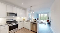 This well-appointed 2-bedroom, 2-bathroom residence is thoughtfully designed across a single floor, offering a bright and modern open-concept layout. The kitchen features crisp white cabinetry, granite countertops, a subway tile backsplash, and a full suite of stainless steel appliances including a gas range, built-in microwave, dishwasher, and refrigerator. A peninsula with seating for two provides a casual dining option and flows seamlessly into the living area, which is bathed in natural light from large sliding glass doors that open to a private balcony overlooking lush greenery. Light-toned hardwood-style flooring runs throughout the main living areas, enhancing the airy feel of the space. The primary bedroom is generously sized, featuring plush carpeting, a large window with outdoor views, and access to a dedicated walk-in closet. The second bedroom is equally comfortable and well-lit. Both bathrooms are finished with granite vanity countertops and white cabinetry, maintaining a consistent, clean aesthetic throughout. A hallway connects the living spaces to the private quarters, adding functional separation. The overall ambiance is clean, contemporary, and welcoming, with a neutral palette that lends itself well to a variety of interior styles.