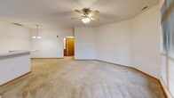The Cabaret floor plan in New Berlin, WI is a thoughtfully designed one-bedroom, one-bathroom unit offering comfortable single-floor living. The open-concept living room is generously sized, featuring plush carpeting, a ceiling fan, and large multi-pane windows dressed with blinds that invite abundant natural light and views of the surrounding neighborhood. The well-appointed kitchen is laid out in a galley style with light oak cabinetry, white countertops, a peninsula with a built-in sink, and black appliances including a refrigerator, range, microwave, and dishwasher. Light wood-style flooring ties the space together cleanly. In-unit laundry hookups are conveniently located just off the kitchen. The spacious primary bedroom continues the carpeted flooring and features a ceiling fan, large windows, and access to a hallway with mirrored closet doors providing ample storage. The full bathroom offers a tiled tub-shower combination with chrome fixtures and tile flooring. The entrance hallway connects smoothly to all areas of the unit. Completing the home is an attached garage with an automatic opener, offering secure and convenient parking alongside additional storage space.