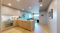 Located at 700 Broadway in Santa Monica, California, this thoughtfully designed one-bedroom, one-bathroom residence offers a refined and modern living experience. Light-toned hardwood flooring flows throughout, lending a warm, cohesive aesthetic across the entire floor plan.

The open-concept kitchen and living area serves as the heart of the home. The kitchen is outfitted with flat-front light wood cabinetry extending to the ceiling, integrated stainless steel appliances, and a generous center island with a ribbed accent panel and white countertops — ideal for both cooking and casual dining. Recessed lighting illuminates the space efficiently.

The living area offers an airy, comfortable atmosphere, anchored by floor-to-ceiling windows and sliding glass doors that open to a private balcony with views of the surrounding Santa Monica neighborhood and its lush palm-lined streets. Natural light fills the space throughout the day.

The spacious primary bedroom features large windows with outdoor views, light wood floors, and ample room for a full furniture suite. Two closets provide generous storage, one of which is a walk-in adorned with vibrant tropical-print wallcovering and built-in shelving.

The bathroom is finished in polished marble-style tile, featuring a wood-framed vanity mirror, a dual-sink vanity with stone countertops, and a glass-enclosed shower — delivering a spa-like experience.