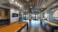 This single-floor amenity space in Smyrna, Tennessee, is a thoughtfully designed game and social lounge that blends contemporary style with recreational functionality. Dark hardwood flooring runs throughout, anchoring the space and contrasting beautifully with the slatted ceiling detail—a defining architectural element that adds depth and visual interest overhead, complemented by recessed lighting and sculptural pendant fixtures.

The game room is well-equipped, featuring a full-size pool table with an amber felt surface, a shuffleboard table, and a ping-pong table, providing a variety of entertainment options. A dedicated lounge area with bar-height seating lines one wall, backed by warm wood paneling, textured wall tile, and mounted flat-screen television, creating a comfortable viewing nook. Decorative moss wall panels and framed artwork add organic and artistic accents throughout.

A wet bar area, complete with a sink, dark cabinetry, and white countertops, makes the space well-suited for social gatherings. Floor-to-ceiling glass walls and double glass doors open directly onto an outdoor terrace, allowing natural light to flood the interior and providing seamless indoor-outdoor connectivity. The overall ambiance is modern and energetic, ideal for community recreation and entertaining.