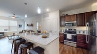 This single-floor residence is thoughtfully designed with an open-concept layout that seamlessly connects the kitchen, dining, and living areas. The kitchen serves as a central hub, showcasing rich dark wood cabinetry, granite countertop surfaces, and a full suite of stainless steel appliances including a refrigerator, range, and built-in microwave. A spacious peninsula with seating for multiple bar stools doubles as a breakfast bar and prep area, enhanced by stylish pendant lighting overhead. Wood-look flooring runs throughout the main living spaces, adding warmth and cohesion to the interior.

The living room is bright and welcoming, featuring multiple windows that allow generous natural light to fill the space. A ceiling fan adds both function and comfort, while a decorative wall-mounted shelf adds character. The bedrooms continue the light, neutral aesthetic, each featuring wood-look flooring, large windows, and ceiling fans for comfort. The primary bedroom benefits from multiple windows that flood the room with natural light.

The bathroom is well-equipped with a granite-topped vanity, rich cabinetry, a tub-shower combination with tile surround, and a walk-in closet, offering both style and practical storage throughout.