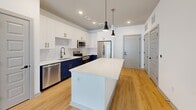 Located at 5944 Highway 92 in Acworth, Georgia, this thoughtfully designed one-bedroom, one-bathroom residence offers a comfortable and modern living experience across a single floor. The open-concept main living area seamlessly combines the kitchen, dining, and living spaces, creating an inviting and functional layout. The kitchen is a standout feature, showcasing bold navy blue lower cabinetry paired with crisp white upper cabinets, gold hardware accents, a classic white subway tile backsplash, and a large central island with a white countertop. A suite of stainless steel appliances — including a range, microwave, dishwasher, and refrigerator — completes the space. Stylish pendant lighting adds a modern finishing touch. Light wood-style flooring runs throughout the main living areas, while the bedroom features plush carpet, a ceiling fan, and a bright window with outdoor views. The bathroom is well-appointed with a navy vanity and a glass-enclosed tile shower. Two closets provide ample storage, including a walk-in closet with wire shelving. Additional highlights include a dedicated pantry, laundry area, utility room, and a private balcony accessible from the living area, bringing in natural light and an outdoor retreat.