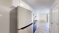 This efficiently designed single-floor unit offers a thoughtfully organized layout that maximizes every square foot. The kitchen is a standout feature, outfitted with crisp white shaker-style cabinetry extending to the ceiling, stainless steel appliances including a refrigerator, electric range, and over-the-range microwave, complemented by sleek stone countertops and a classic white subway tile backsplash. A stainless steel undermount sink adds a polished finishing touch.

Light wood-style luxury flooring flows continuously from the kitchen into the living room, creating a cohesive and open feel. The living room is bright and airy, benefiting from a large sliding glass door that frames a view of lush greenery and opens directly onto a private balcony. A wall-mounted HVAC unit ensures year-round comfort in this space.

The bathroom is designed with accessibility in mind, featuring a roll-in shower with sturdy grab bars, a curtain enclosure, a wall-mounted sink, and clean tile flooring. Additional spaces include a closet for storage and a dedicated utility room. The overall palette of neutral whites and warm beige tones, paired with clean lines and modern finishes, gives the unit a fresh, contemporary ambiance.
