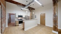 Located at 237-243 Furnace St in Akron, Ohio, this one-bedroom, one-bathroom unit offers a compelling mix of historic industrial character and contemporary updates. The open layout makes efficient use of its footprint, with light wood-style flooring flowing through the main living and kitchen areas.

The kitchen is a standout feature, boasting stainless steel appliances including a range, over-the-range microwave, and refrigerator, paired with crisp white upper cabinetry, warm wood-toned lower cabinets, and white quartz countertops. A tile backsplash adds texture, while an exposed structural column and original brick walls lend unmistakable industrial charm. Soaring ceiling heights amplify the sense of space throughout.

The bedroom features plush carpeting, a double-door closet, and dramatic exposed brick walls that rise to tall ceilings, with natural light entering through a window. The room's loft-like character is enhanced by visible ductwork and original building elements.

The bathroom is clean and functional, featuring a soaking tub with subway tile surround, a toilet, and a vanity with wood cabinetry. A hallway connects the rooms, providing practical flow throughout the unit. This space is ideal for those who appreciate historic building character combined with modern conveniences in the heart of Akron.