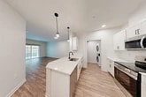 Located at 1061 Dryden Rd in Ithaca, NY, this thoughtfully designed single-story home offers a clean, modern aesthetic throughout its well-utilized floor plan. The heart of the home is an open-concept living, dining, and kitchen area bathed in natural light from a sliding glass door that leads to the outdoors. The kitchen is a standout feature, showcasing crisp white shaker cabinetry, a large quartz waterfall island with an undermount sink and matte black faucet, stainless steel appliances including a range, microwave, and refrigerator, and stylish pendant lighting overhead. Light wood-tone flooring runs throughout the main living areas, complementing the bright, neutral palette. A dedicated laundry closet with a stacked washer and dryer is conveniently tucked just off the kitchen. The bedroom is a comfortable retreat featuring plush carpeting, a ceiling fan, and access to a closet and a full bathroom with a soaking tub. A second bathroom provides added convenience. Two closets offer generous storage throughout. The attached garage rounds out this home's practical offerings, providing secure parking and additional storage space in a well-maintained, move-in ready setting.