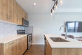 Located at 98 Farley Drive in Guelph, Ontario, this efficiently designed studio unit makes excellent use of its compact footprint across a single floor. The open-concept layout connects the kitchen and living area seamlessly, creating a bright and functional living environment.

The kitchen is a standout feature, boasting warm wood-tone cabinetry, a white quartz peninsula with seating for two, stainless steel appliances including a refrigerator, electric range, and built-in microwave, a subway tile backsplash, and a striking industrial-style pendant light fixture above the island.

The living area is flooded with natural light through large floor-to-ceiling windows and a glass door that opens onto a private balcony with views of the surrounding Guelph cityscape. A built-in Murphy bed with integrated white cabinetry provides a smart, space-saving sleeping solution. The living space also accommodates a wall-mounted television and a media console, alongside comfortable seating.

Throughout the unit, wood-look flooring adds warmth and continuity. The bathroom features a glass-enclosed shower with clean white tile surround and hardwood-style flooring. A dedicated hallway connects all areas, with in-suite laundry conveniently tucked away. The unit's modern, neutral palette and thoughtful design make it a highly functional urban living space.
