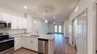 This single-floor unit offers a clean, contemporary design centered around an open-concept layout. The kitchen serves as the heart of the space, featuring a large granite-topped island with a double sink, white shaker-style cabinetry, stainless steel appliances including a refrigerator, range, microwave, and dishwasher, and elegant pendant lighting overhead. Recessed lighting complements the bright, neutral color palette throughout. The kitchen flows seamlessly into the living area, which is generously sized and bathed in natural light from a set of double glass doors. A ceiling fan adds both function and style to this inviting common area. Wood-look plank flooring runs consistently throughout the entire unit, adding warmth and visual continuity. The bedrooms are well-proportioned, each featuring ceiling fans, natural light from windows with blinds, and ample wall space. A hallway connects the private quarters, providing a logical separation between living and sleeping areas. The bathrooms are finished with white vanity cabinetry, brushed nickel hardware, and wood-look flooring. One bathroom includes a walk-in glass-door shower with built-in shelving. A laundry area with washer and dryer is also present. The overall ambiance is bright, clean, and move-in ready.