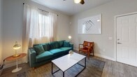 This single-floor residence offers a thoughtfully designed layout with a cohesive modern aesthetic throughout. The living room serves as a welcoming focal point, featuring wood-look flooring, a ceiling fan, and a window dressed with sheer curtains that allow natural light to fill the space. The dining area is positioned adjacent to a sliding glass door that opens to an outdoor view, providing a bright and airy atmosphere ideal for everyday meals or entertaining. The kitchen is well-equipped with two-tone cabinetry — white upper cabinets paired with gray lower cabinets — complemented by white quartz countertops, a classic subway tile backsplash, and stainless steel appliances including a range, microwave, and dishwasher. The bedroom is a calm retreat with plush carpeting, neutral walls, and a window with vertical blinds. The bathroom features a white vanity with ample counter space, a large mirror, and a shower-tub combination. A dedicated laundry area houses a full-sized washer and dryer with overhead shelving for added storage. Throughout the residence, neutral tones and clean lines create a consistent, modern ambiance that is both functional and inviting.