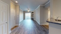 Located at 6100 Avery Dr in Fort Worth, TX, this single-floor unit offers a thoughtfully designed layout with a neutral color palette and a blend of hard and soft flooring surfaces. The living area serves as the centerpiece of the space, showcasing rich wood-style plank flooring, crown molding, and a ceiling fan with light fixture. A sliding glass door with vertical blinds allows natural light to fill the room while providing outdoor access. A distinctive arched built-in shelving niche adds architectural character to the living area, offering both display and storage functionality.

The kitchen is positioned adjacent to the living space and features a peninsula with a contrasting countertop, white cabinetry, and a full suite of appliances including a refrigerator, microwave, and range. Track lighting overhead adds focused illumination to the workspace. The flooring in this area transitions to a lighter wood-style surface.

The bedroom is carpeted for comfort and includes a window with horizontal blinds that allows natural light and outdoor views. The bathroom is clean and functional, equipped with a tub-shower combination, tile surround, wood-look flooring, and brushed nickel hardware. Crown molding and consistent neutral tones tie the overall aesthetic of the space together cohesively.