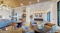 Located at 229 East Chatham Street in the heart of downtown Cary, NC, this expansive single-floor amenity space offers a thoughtfully designed environment that blends contemporary style with functional versatility. The welcoming lobby greets visitors with herringbone wood-look flooring, soaring ceilings, rich burnt-orange velvet lounge chairs, and a sleek elevator, with direct access to a private mailroom featuring decorative tilework and a green accent wall.

The open-plan living and social area is a standout, defined by a striking warm wood ceiling, a globe chandelier installation, and floor-to-ceiling black-framed glass walls that invite abundant natural light and views of an outdoor courtyard. Open black metal shelving units with curated greenery elegantly divide distinct seating zones without obstructing sightlines. A dramatic fireplace wall clad in rich textured stone anchors the living lounge, complete with comfortable sofas and a live-edge wood coffee table.

The dining area features a substantial wood communal table and access to the courtyard via glass doors, while semi-private booth seating with black metal framing and pendant lighting provides intimate spaces for focused work or casual gatherings. Throughout, the herringbone flooring, arched architectural details, and curated artwork create a cohesive, upscale ambiance suited for both community connection and productivity.