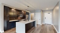 Located at 50 S. Grant in Columbus, Ohio, this well-appointed 2-bedroom, 2-bathroom residence offers a thoughtfully designed single-floor layout with modern finishes throughout. The open-concept living and kitchen area serves as the heart of the home, anchored by a striking kitchen island with a white quartz countertop, matte black fixtures, and an integrated sink. Dark cabinetry with a textured tile backsplash pairs elegantly with stainless steel appliances, while an industrial-style pendant light fixture adds a refined touch overhead. Wide-plank hardwood flooring flows seamlessly through the main living areas, complementing the neutral warm-toned walls. The living room benefits from large windows that invite abundant natural light and views of the surrounding neighborhood. Both bedrooms feature hardwood-style flooring, recessed lighting, and neutral paint tones. The primary bedroom includes a dedicated walk-in closet with built-in shelving and hanging storage. The second bedroom also features its own closet with organized storage. The bathrooms are finished with large-format tile flooring, a glass-enclosed walk-in shower with white subway tile, black metal hardware accents, and clean white vanities. A connecting hallway and two closets complete this efficient, contemporary floor plan.
