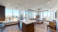 Located in the heart of downtown Dallas, this single-floor high-rise residence at 1401 Pacific Ave offers a refined urban living experience defined by sweeping panoramic views of the Dallas skyline, including the iconic Fountain Place tower. The open-concept design seamlessly connects the kitchen, dining, and living areas, all framed by expansive floor-to-ceiling windows that flood the space with natural light.

The kitchen is a standout feature, appointed with rich walnut cabinetry, stainless steel appliances, a built-in wine cooler, and a generously sized island topped with a striking veined quartz countertop and bar seating. The living area is equally impressive, with ceiling fans, recessed lighting, and unobstructed city views that serve as a dramatic backdrop.

A long gallery-style hallway, finished with light hardwood flooring and illuminated by recessed ceiling lights, connects the living spaces to the private quarters, and is accented with curated artwork. The bedroom enjoys carpeted flooring and floor-to-ceiling windows showcasing breathtaking skyline views. The primary bathroom features a dual-sink vanity with a gold-framed mirror and tile flooring. Additional conveniences include a walk-in closet and an in-unit laundry room with full-size washer and dryer.