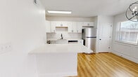 Located at 4015 Estermarie Dr in Cincinnati, Ohio, this thoughtfully designed 2-bedroom home offers a clean, modern aesthetic across a single floor. The open-concept kitchen and living area serves as the heart of the space, showcasing white shaker cabinetry, a white quartz peninsula island, stainless steel appliances including a refrigerator, dishwasher, microwave, and range, and a sleek matte black faucet at the sink. Warm-toned hardwood-style flooring flows throughout the entire home, tying each room together cohesively. The living area features decorative wainscoting, a white painted brick accent wall, a ceiling fan with light, and a sliding glass door that invites natural light and outdoor views. An elegant orb chandelier adds a stylish touch to the dining area. The primary bedroom is generously sized, complete with dual sliding closets and its own ceiling fan. The second bedroom also features a ceiling fan and a window that provides natural light. A connecting hallway links the bedrooms to the main living areas. The home's bright white walls, modern fixtures with matte black hardware, and consistent flooring create a fresh, contemporary ambiance throughout.