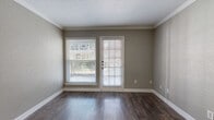 Located at 13110 Kuykendahl Rd in Houston, TX, this single-floor unit offers a well-organized layout with a variety of finishes throughout. The main living area features rich, dark hardwood-style flooring and is finished with crown molding along the ceiling. A large window paired with a glass-panel exterior door floods the space with natural light and provides direct outdoor access, making the area feel open and connected to the outside. Neutral taupe-toned walls throughout create a clean, cohesive aesthetic.

The kitchen is equipped with black appliances, including an electric range, over-the-range microwave, and a sink with dark countertops, all set atop wood-look flooring. White cabinetry provides ample storage, and a door off the kitchen offers additional convenience.

The bedrooms feature wall-to-wall carpet and ceiling fans, offering a comfortable and quiet environment. Each bedroom includes window blinds that allow for natural light and privacy control. Additional areas of the unit display hardwood-style flooring with crown molding, a wall-mounted thermostat, and built-in HVAC venting. The bathroom includes a full tub-shower combination with white tile surround and chrome fixtures, maintaining a clean and functional design throughout.
