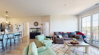 Located at 140 E Monument Ave in Dayton, Ohio, this single-floor residence offers a well-designed, modern layout that balances comfort and functionality. The open-concept living area is bright and inviting, featuring light-toned flooring, neutral walls, and large sliding glass doors that lead to a private balcony with outdoor views — allowing natural light to pour into the space.

The kitchen is a standout feature, outfitted with crisp white cabinetry, quartz countertops, stainless steel appliances, and a generous island with bar seating. Pendant lighting above the island adds a contemporary touch, while ample cabinetry and counter space make it highly practical.

The unit includes two bedrooms, each carpeted and filled with natural light from sizable windows that overlook the balcony and surrounding area. Both bathrooms are finished with white shaker-style cabinetry, quartz countertops, and wood-look flooring, maintaining a clean and cohesive aesthetic throughout.

The living room comfortably accommodates a full seating arrangement and connects seamlessly to the balcony, reinforcing the home's airy, open feel. Throughout the residence, consistent finishes — including light wood-look flooring in common areas and bathrooms — create a unified, modern design from entry to bedroom.