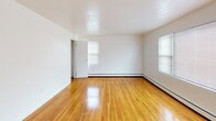 This single-floor unit at 152 Manor Pkwy in Rochester, NY offers a straightforward, functional layout with classic design elements throughout. The living areas are defined by warm, polished hardwood floors that extend through the main living space and bedrooms, reflecting natural light that enters through multiple windows fitted with blinds. Baseboard heating units run along the walls in the living areas and bedrooms, providing consistent warmth throughout the cooler Rochester seasons.

The kitchen features white cabinetry with ample upper and lower storage, a coil-burner electric range, a full-size refrigerator, and a stainless steel sink set into a laminate countertop. The tile flooring in the kitchen provides a practical, easy-to-clean surface. The bedrooms continue the hardwood flooring theme; one bedroom includes a reach-in closet with a hanging rod, while both rooms benefit from natural light through window openings.

The bathroom is equipped with a full soaking tub and tiled surround in a neutral palette of white and beige, complemented by a window that allows natural ventilation. The overall aesthetic of the unit is clean and neutral, with white walls throughout creating a bright, open atmosphere well-suited for personalization.