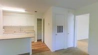 Located at 3500 Creighton Rd in Pensacola, Florida, this single-floor residence offers a practical and well-organized layout designed for comfortable everyday living. The kitchen is outfitted with white cabinetry that extends to the upper walls, providing generous storage space, along with light-toned countertops and a built-in sink. A kitchen island or peninsula adds additional workspace and helps define the transition between the kitchen and adjacent living areas. A dedicated walk-in pantry off the kitchen offers substantial shelving, making it ideal for organized storage of pantry goods and household essentials. The flooring throughout the space features a combination of warm hardwood in the kitchen and dining areas, transitioning to plush carpet in the living and hallway spaces, adding a sense of comfort underfoot. The walls are finished in a clean, neutral white throughout, contributing to a bright and open atmosphere. A hallway leads to additional rooms, with multiple doors suggesting private spaces such as bedrooms or utility closets. HVAC venting is integrated into the wall, reflecting a thoughtfully planned interior. Overall, the space presents a clean, move-in ready environment well-suited for functional residential living in the Pensacola area.