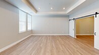 This thoughtfully designed one-bedroom, one-bathroom unit at 298 W Monroe St, Unit 403 in Dundee, Michigan offers a clean, modern aesthetic throughout its well-utilized floor plan. The open-concept kitchen and living area serves as the heart of the unit, featuring dark wood-grain cabinetry that extends floor to ceiling, white quartz countertops, a stainless steel undermount sink with a matte black faucet, and a full suite of stainless steel appliances including a refrigerator with ice maker, range, microwave, and dishwasher. Light wood-style vinyl plank flooring runs continuously throughout the space, lending warmth and cohesion. The living area benefits from recessed lighting and natural light from large windows fitted with blinds. A distinctive tray ceiling adds architectural depth to the space. The bedroom is a comfortable size, also featuring a tray ceiling, recessed lighting, and windows that allow natural light to filter in. Stylish sliding barn doors connect the bedroom to an adjacent closet and hallway, adding a modern design element. The closet provides organized storage space. The bathroom is finished with neutral tones and matte black hardware accents consistent with the unit's overall design language. Clean lines, contemporary finishes, and a neutral color palette define this well-appointed Dundee residence.