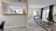 Located at 12801 Indian School Rd NE in Albuquerque, New Mexico, this one-bedroom, one-bathroom residence offers a thoughtfully arranged single-floor layout. Light gray walls, wood-style flooring, and recessed lighting create a clean, modern aesthetic throughout the main living areas. The open-concept living and dining area is bright and welcoming, featuring a sliding glass door that leads to a private outdoor patio, allowing natural light to flow freely into the space. Built-in shelving adds functional character to the living room. The galley-style kitchen is efficiently designed with white cabinetry, stainless steel appliances including a range and dishwasher, and a pass-through counter that connects to the dining and living areas. The dining nook comfortably accommodates a small table and chairs. The bedroom is a comfortable retreat, featuring plush carpeting, a ceiling fan, and a large window with a built-in sill, providing ample natural light and a cozy reading spot. A dedicated closet offers convenient storage. The bathroom includes a single vanity with white cabinetry, a granite-style countertop, and a full tub-shower combination with tile surround. A hallway connects the living spaces to the private quarters, contributing to the overall functional flow of the home.