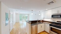 Located at 7 Cameron Ave in Cambridge, MA, this one-bedroom, one-bathroom residence offers a well-designed open-concept layout with modern finishes throughout. The living room is bright and airy, featuring light-toned hardwood floors, a contemporary track lighting fixture, and expansive floor-to-ceiling sliding glass doors that open to a private balcony overlooking lush green trees — filling the space with abundant natural light.

The kitchen flows seamlessly from the living area and is appointed with crisp white shaker cabinetry, rich dark granite countertops, a white subway tile backsplash, and a full suite of stainless steel appliances including a gas range, built-in microwave, dishwasher, and refrigerator. Pendant lighting above the kitchen peninsula adds a stylish, functional touch.

The bedroom is a comfortable, carpeted retreat featuring a large window with views of the surrounding neighborhood and ample room for furnishings. The full bathroom is clean and well-appointed, with large-format tile flooring, white cabinetry with granite counters, and a full soaking tub with shower. Throughout the residence, neutral tones and quality materials create a cohesive, modern aesthetic suited for comfortable urban living in the heart of Cambridge.