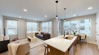 This well-designed single-floor residence offers two bedrooms and two bathrooms within a thoughtfully arranged floor plan. The open-concept living area seamlessly connects the kitchen, dining, and living spaces, all finished with light wood-tone flooring that runs consistently throughout. Large windows fitted with horizontal blinds flood the common areas with natural light and provide views of the surrounding urban landscape.

The kitchen is a standout feature, anchored by a generous island with a white quartz countertop, an undermount sink, and seating for multiple guests. Warm wood cabinetry, stainless steel appliances, a subway tile backsplash, and pendant lighting complete the space. Adjacent to the kitchen, the dining area benefits from a corner window arrangement, enhancing its bright, airy feel.

The primary bedroom is a comfortable retreat, featuring a ceiling fan, a large window, and direct access to a dedicated bathroom. That bathroom includes a wood-toned vanity with quartz countertops, matte black fixtures, and a walk-in closet with wire shelving systems. The second bedroom mirrors similar finishes and appointments.

Connecting hallways are clean and well-proportioned, maintaining a cohesive, modern aesthetic throughout the residence.