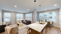 This well-designed single-floor residence offers two bedrooms and two bathrooms within a thoughtfully arranged floor plan. The open-concept living area seamlessly connects the kitchen, dining, and living spaces, all finished with light wood-tone flooring that runs consistently throughout. Large windows fitted with horizontal blinds flood the common areas with natural light and provide views of the surrounding urban landscape.

The kitchen is a standout feature, anchored by a generous island with a white quartz countertop, an undermount sink, and seating for multiple guests. Warm wood cabinetry, stainless steel appliances, a subway tile backsplash, and pendant lighting complete the space. Adjacent to the kitchen, the dining area benefits from a corner window arrangement, enhancing its bright, airy feel.

The primary bedroom is a comfortable retreat, featuring a ceiling fan, a large window, and direct access to a dedicated bathroom. That bathroom includes a wood-toned vanity with quartz countertops, matte black fixtures, and a walk-in closet with wire shelving systems. The second bedroom mirrors similar finishes and appointments.

Connecting hallways are clean and well-proportioned, maintaining a cohesive, modern aesthetic throughout the residence.
