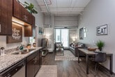 This contemporary single-floor unit offers a thoughtfully designed layout that blends functionality with modern style. The open-concept living and dining area is a standout space, boasting soaring ceilings with exposed ductwork that lend an industrial-chic character, and large windows that flood the room with natural light. Durable wood-look flooring anchors the living space, while plush carpet carries through the bedrooms.

The kitchen is efficiently designed, featuring rich dark wood cabinetry, granite countertops, a double sink, and a full suite of stainless steel appliances including a refrigerator, electric range, microwave, and dishwasher. The kitchen flows seamlessly into the living and dining areas, making it ideal for everyday living.

Each bedroom offers a comfortable, carpeted retreat with ample room for a bed, dresser, and a dedicated desk workspace. Closet storage with wire shelving adds practicality, and large windows with blinds allow for adjustable natural light.

The bathrooms are finished with tile flooring, granite-topped dark wood vanities, and large mirrors, reflecting the same design language found throughout the unit. The overall ambiance is modern and inviting, with an industrial edge introduced by the exposed mechanical elements visible in the living area.