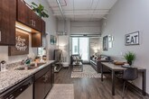 This contemporary single-floor unit offers a thoughtfully designed layout that blends functionality with modern style. The open-concept living and dining area is a standout space, boasting soaring ceilings with exposed ductwork that lend an industrial-chic character, and large windows that flood the room with natural light. Durable wood-look flooring anchors the living space, while plush carpet carries through the bedrooms.

The kitchen is efficiently designed, featuring rich dark wood cabinetry, granite countertops, a double sink, and a full suite of stainless steel appliances including a refrigerator, electric range, microwave, and dishwasher. The kitchen flows seamlessly into the living and dining areas, making it ideal for everyday living.

Each bedroom offers a comfortable, carpeted retreat with ample room for a bed, dresser, and a dedicated desk workspace. Closet storage with wire shelving adds practicality, and large windows with blinds allow for adjustable natural light.

The bathrooms are finished with tile flooring, granite-topped dark wood vanities, and large mirrors, reflecting the same design language found throughout the unit. The overall ambiance is modern and inviting, with an industrial edge introduced by the exposed mechanical elements visible in the living area.