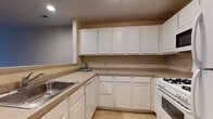 Located at 156 Somerset Ln in Avon Lake, Ohio, this single-floor residence offers a practical and well-organized layout designed for comfortable everyday living. The kitchen is a standout feature, outfitted with an abundance of white raised-panel cabinetry that extends to the ceiling, providing generous storage. Neutral laminate countertops run along a U-shaped configuration, complemented by a stainless steel sink, a white gas range, built-in microwave, and a dishwasher. Light tile flooring anchors the kitchen space, which opens directly to the main living area via a peninsula with a contrasting blue-gray accent panel — an ideal spot for casual dining or meal prep. The open-concept living area is spacious and bright, featuring warm carpeting, recessed and flush-mount lighting, and a neutral color palette that creates a clean, inviting atmosphere. A built-in desk nook near the hallway adds functional workspace. The bedrooms are generously proportioned, each with soft carpeting, closet access, and windows that bring in natural light. Textured ceilings appear throughout portions of the home, adding subtle architectural character. The overall design is understated and move-in ready, offering a comfortable layout in a residential Avon Lake setting.