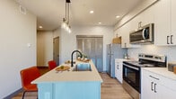Located at 12115 State Ave in Marysville, WA, this well-designed single-floor residence offers a thoughtfully laid-out living space with modern finishes throughout. The open-concept kitchen serves as the heart of the home, showcasing a light blue center island with a deep undermount sink, matte black faucet, and sleek quartz countertops. White shaker cabinetry extends to the ceiling for ample storage, complemented by stainless steel appliances including a refrigerator, range, and over-the-range microwave. Pendant lighting above the island adds a warm, stylish touch, while louvered sliding doors provide a distinctive design accent. The living area is bathed in natural light through large windows that frame views of the surrounding neighborhood. The space is open and inviting, with light wood-look flooring flowing throughout. The bedroom is a comfortable retreat featuring multiple windows that allow abundant daylight, along with a sliding closet door offering generous storage. The bathroom is finished with large-format tile flooring, a modern vanity with clean-lined cabinetry, a wide mirror, and contemporary light fixtures with matte black hardware accents, completing this cohesive and well-appointed residence.